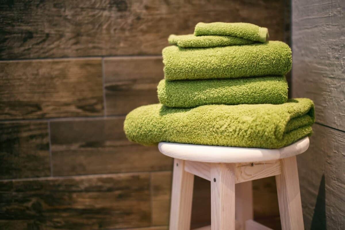 Wooden stool with stack of lime green bath towels on top.