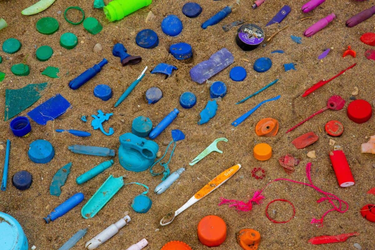 Reduce plastic use: sand with plastic trash arranged in rainbow-like colors.
