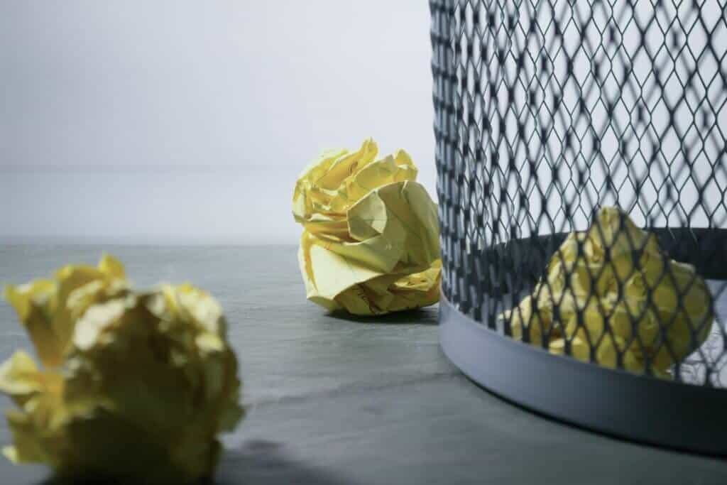 Reducing paper waste: Mesh trash can with balled up yellow lined paper.