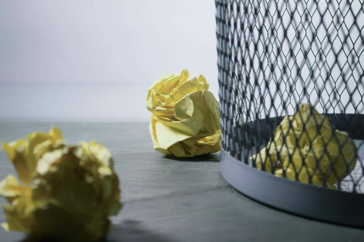 Mesh trash can with balled up yellow lined paper.