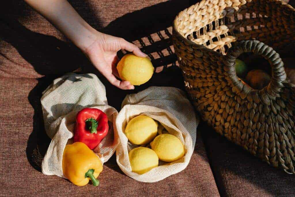 person's hand holding a piece of fruit above more produce inside a reusable mesh produce bag