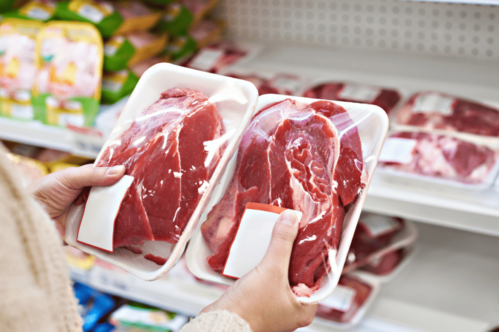 person holding packages of beef in a grocery store