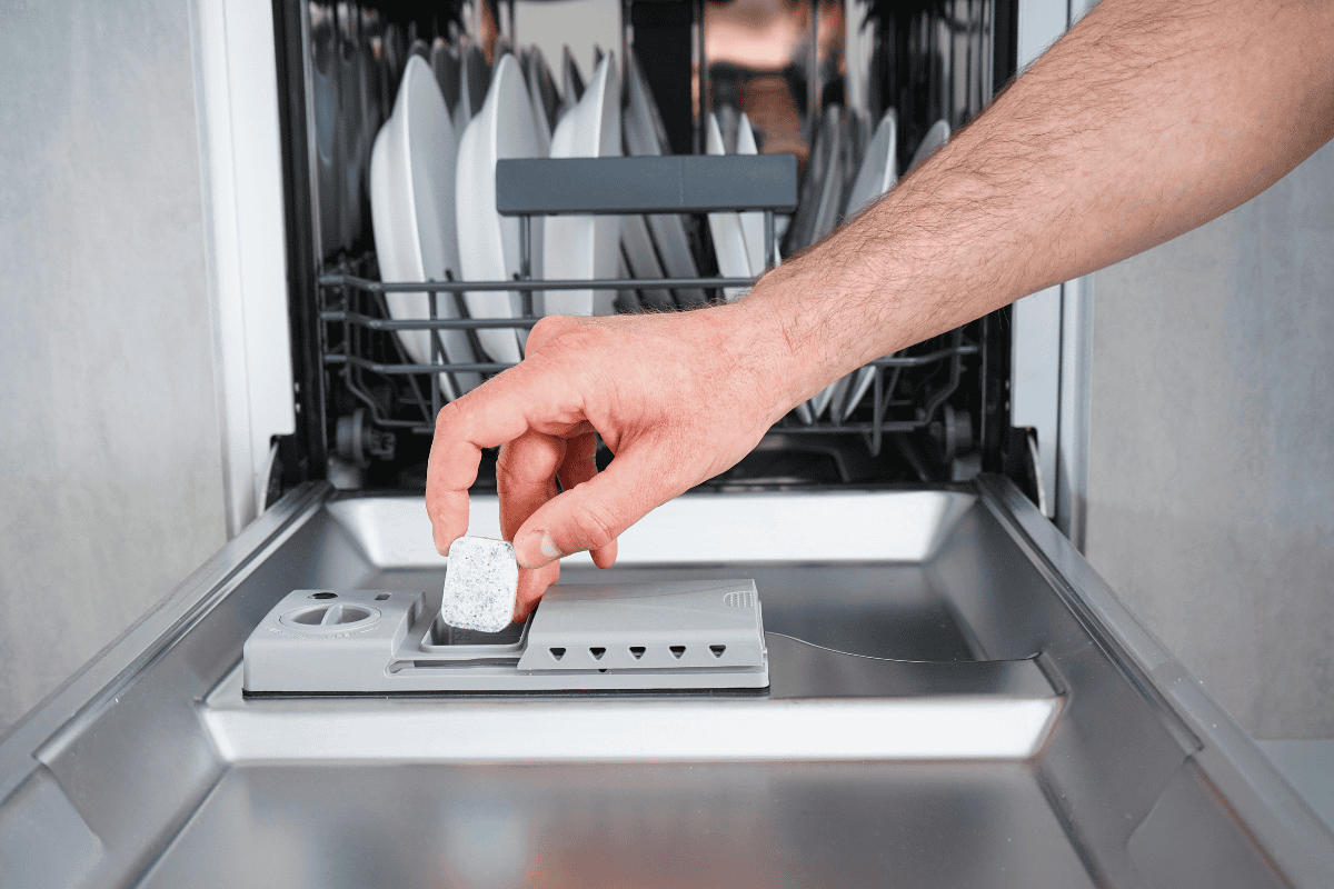 Hand placing non-toxic dishwasher detergent tablet into compartment on dishwasher door